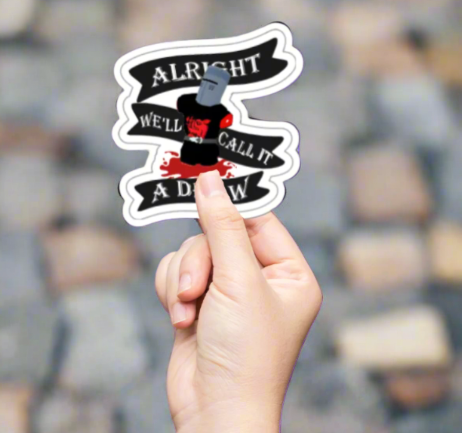 A hand holding a die-cut sticker with the Monty Python Black Knight theme, featuring white and red text on a black background.